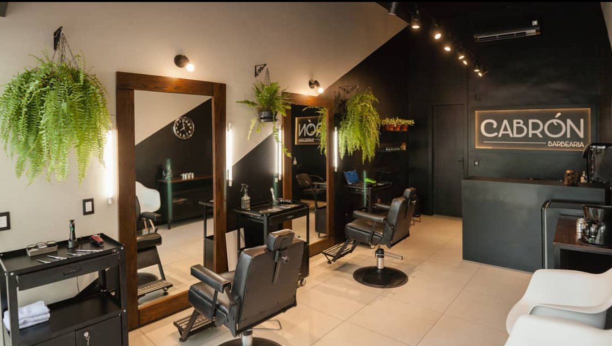 Recepção da barbearia com espelhos, plantas e letreiro Cabrón